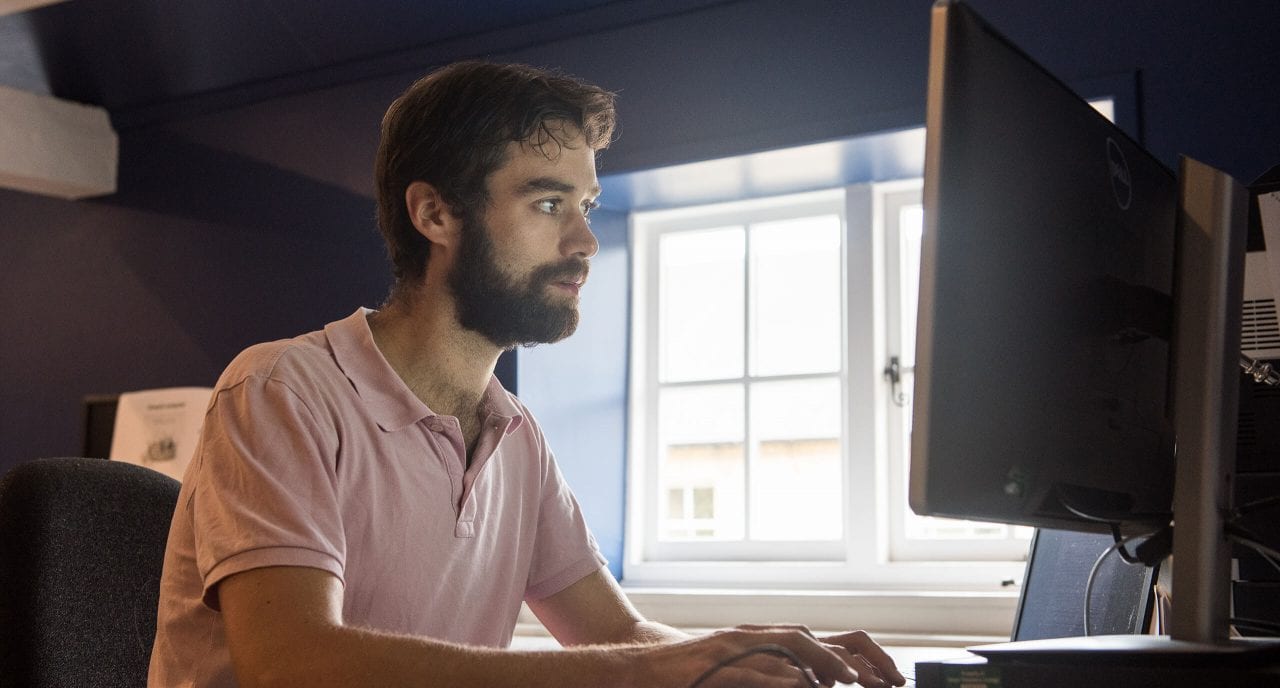 A male student in a pink polo shirt types on a keyboard as he looks at a monitor screen in the Hayloft at Green Templeton College