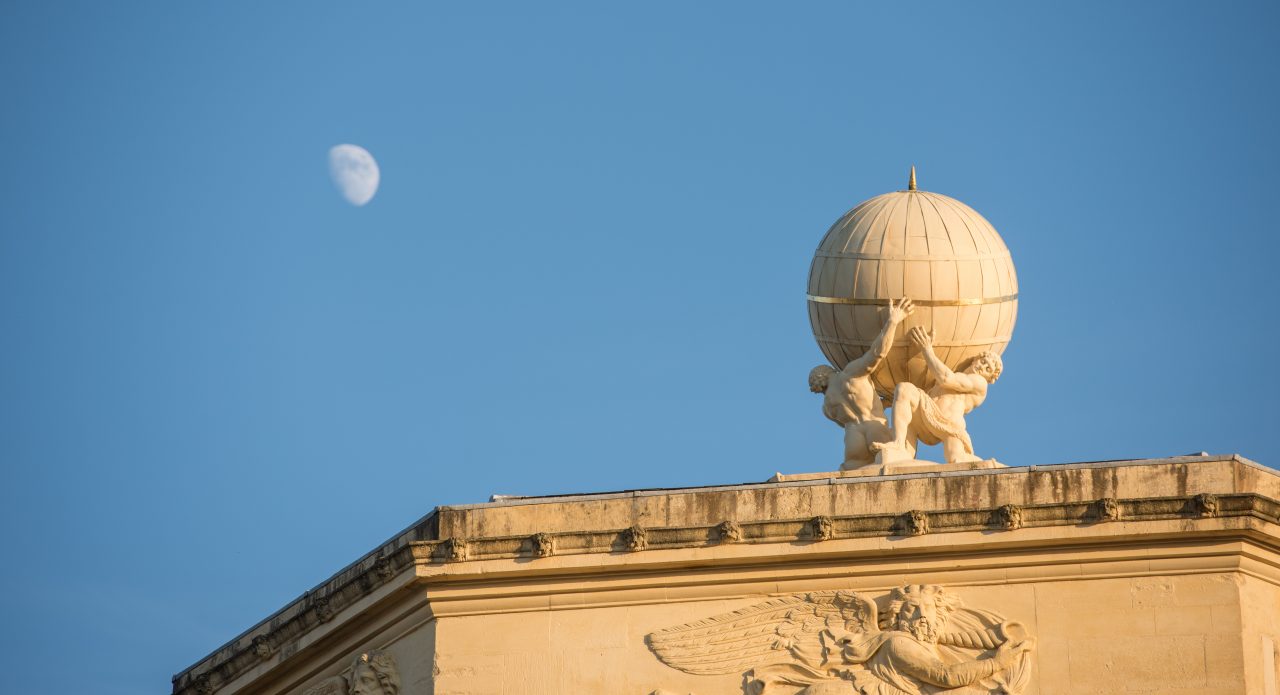 The moon is seen against the globe at the top of the Radcliffe Observatory at sunset