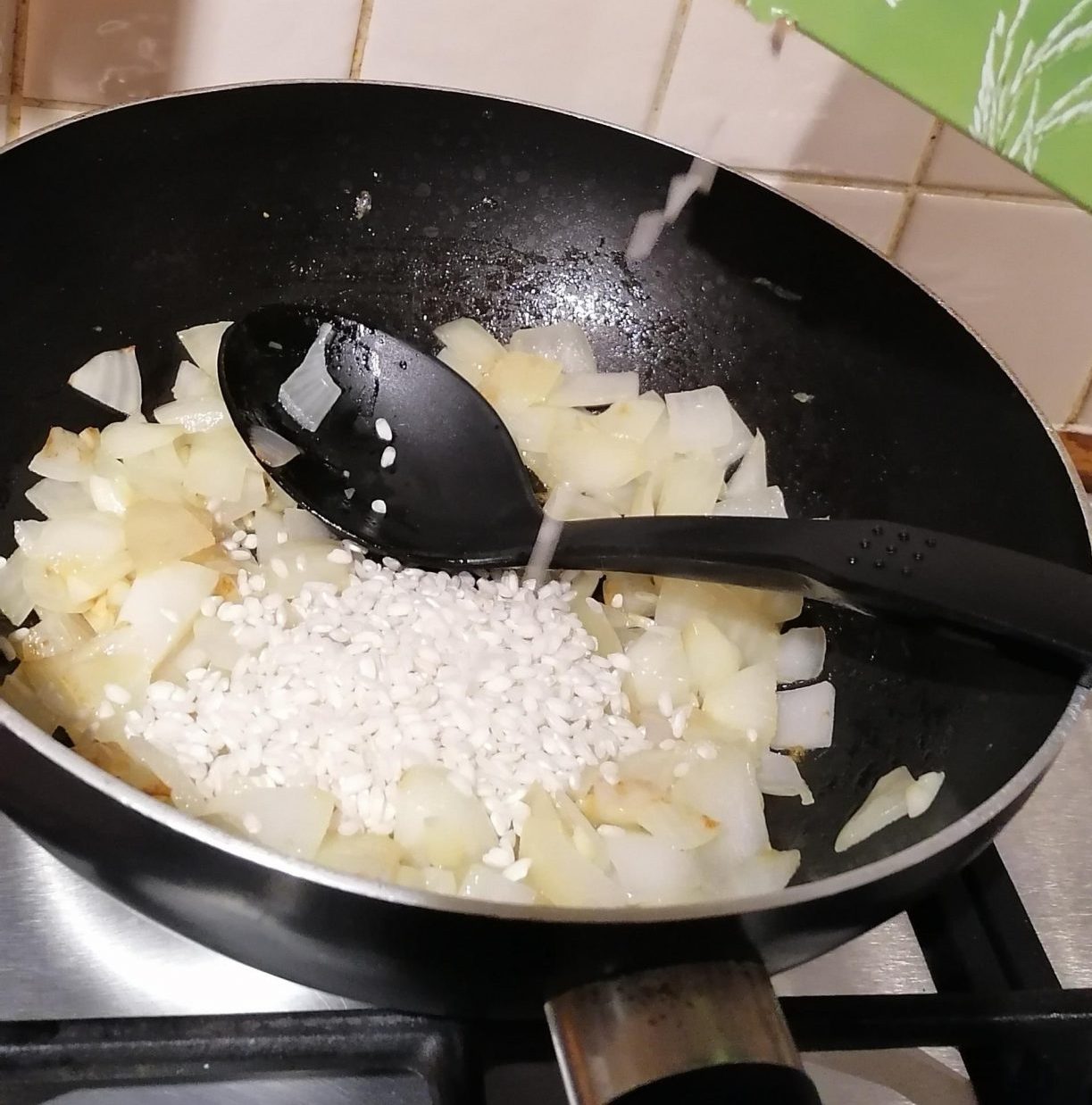 A packet of Arborio rice being poured into a mixture of softened onion and garlic