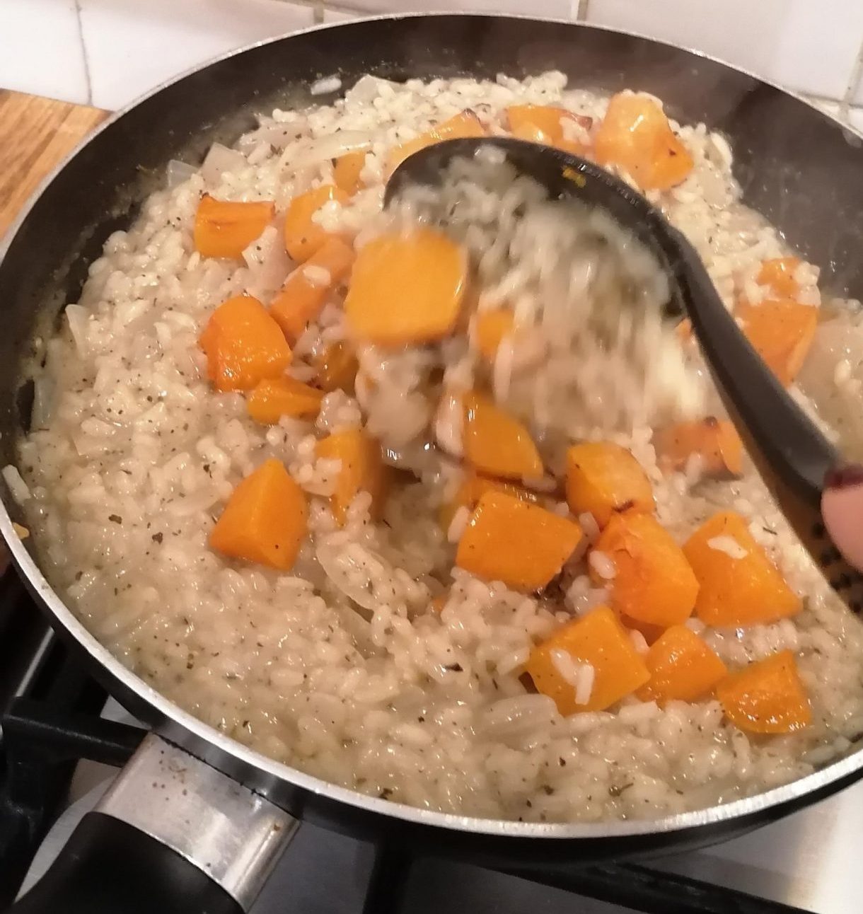 Chunks of roasted butternut squash being stirred into a creamy risotto mixture