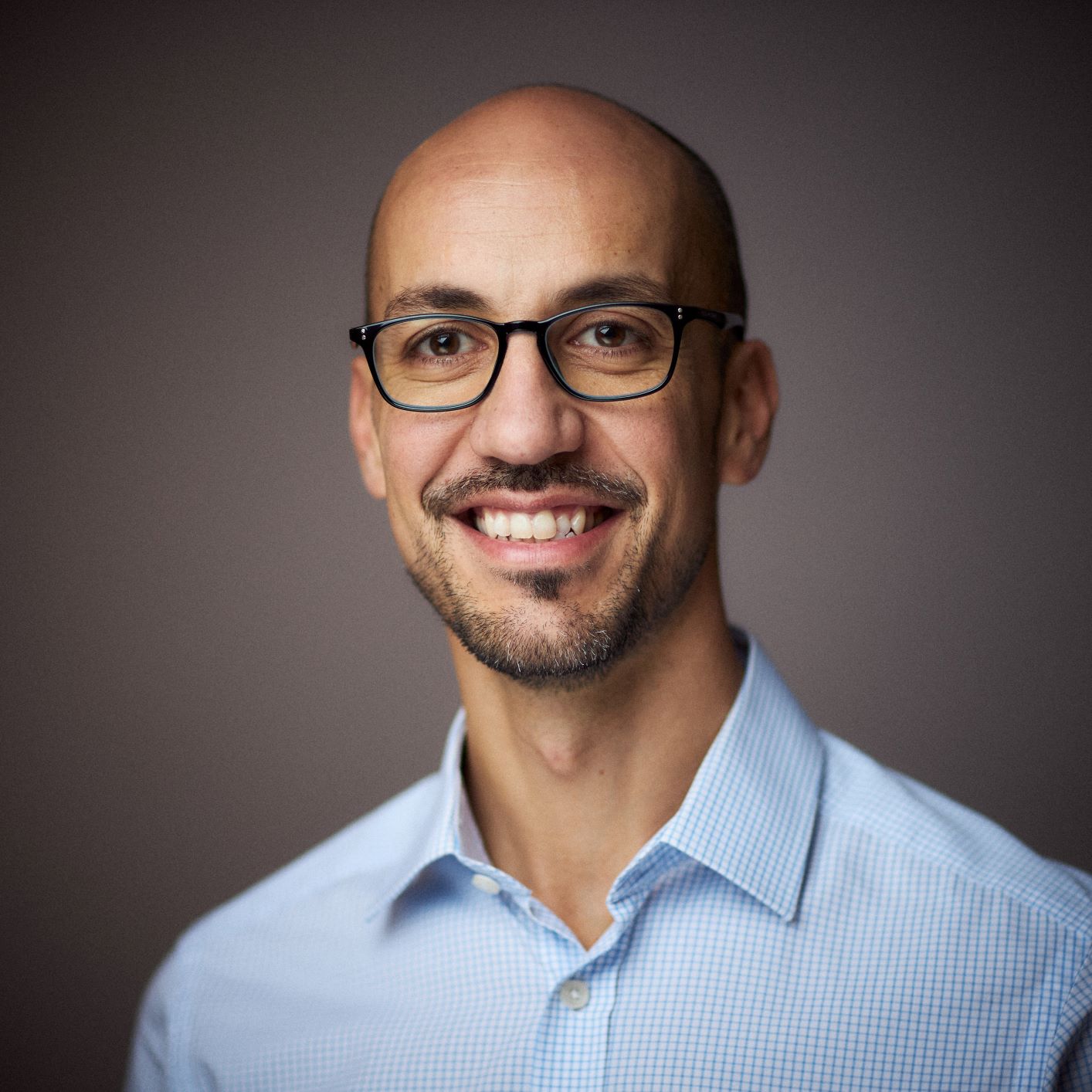 Green Templeton College Clinical Medicine DPhil student Davide Bilardi is smiling and wearing a blue open-necked shirt and glasses