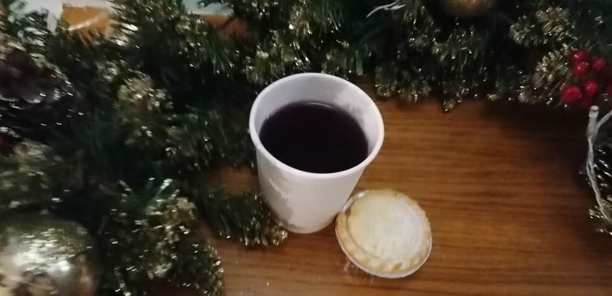 A cup of mulled wine and a mince pie on a table next to Christmas decorations