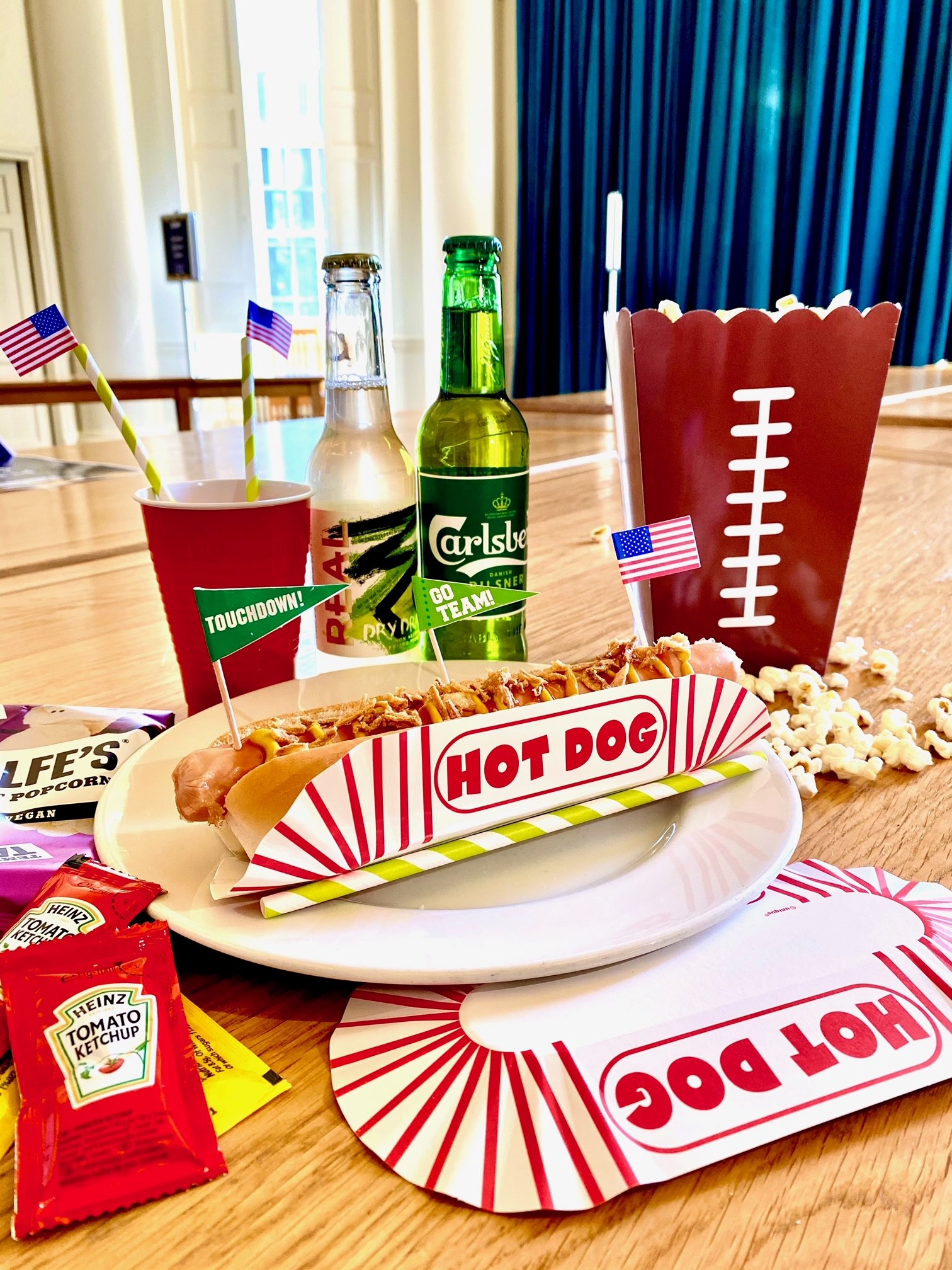 The contents of a Super Bowl Event Kit containing a hot dog, drinks, sauces, popcorn and miniature American flags