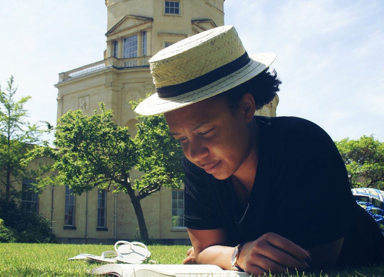 A student reads a book in the sunshine while lying on the grass outside the Radcliffe Observatory