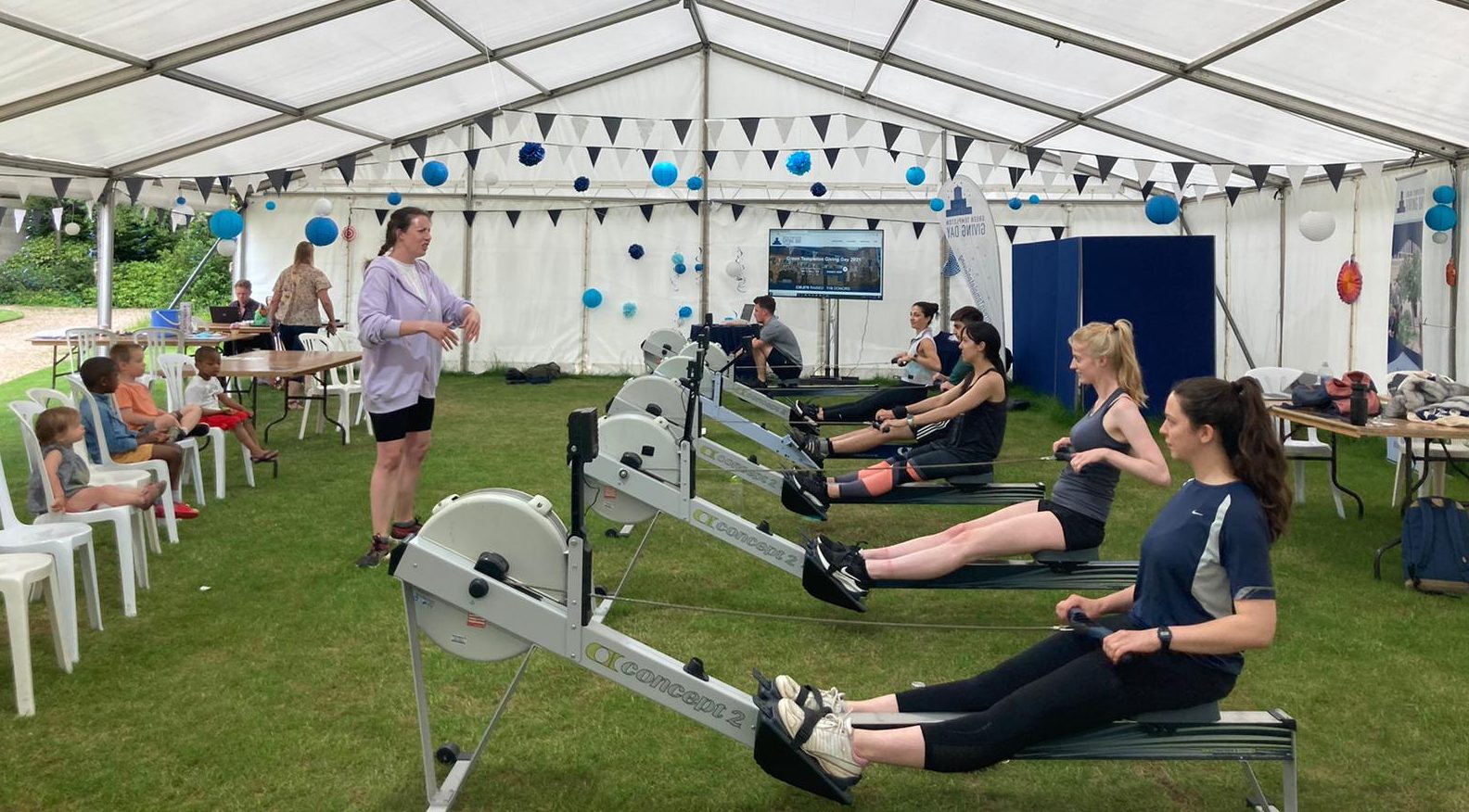 A group of children sit on seats watching the GTCWBC rowing in the marquee