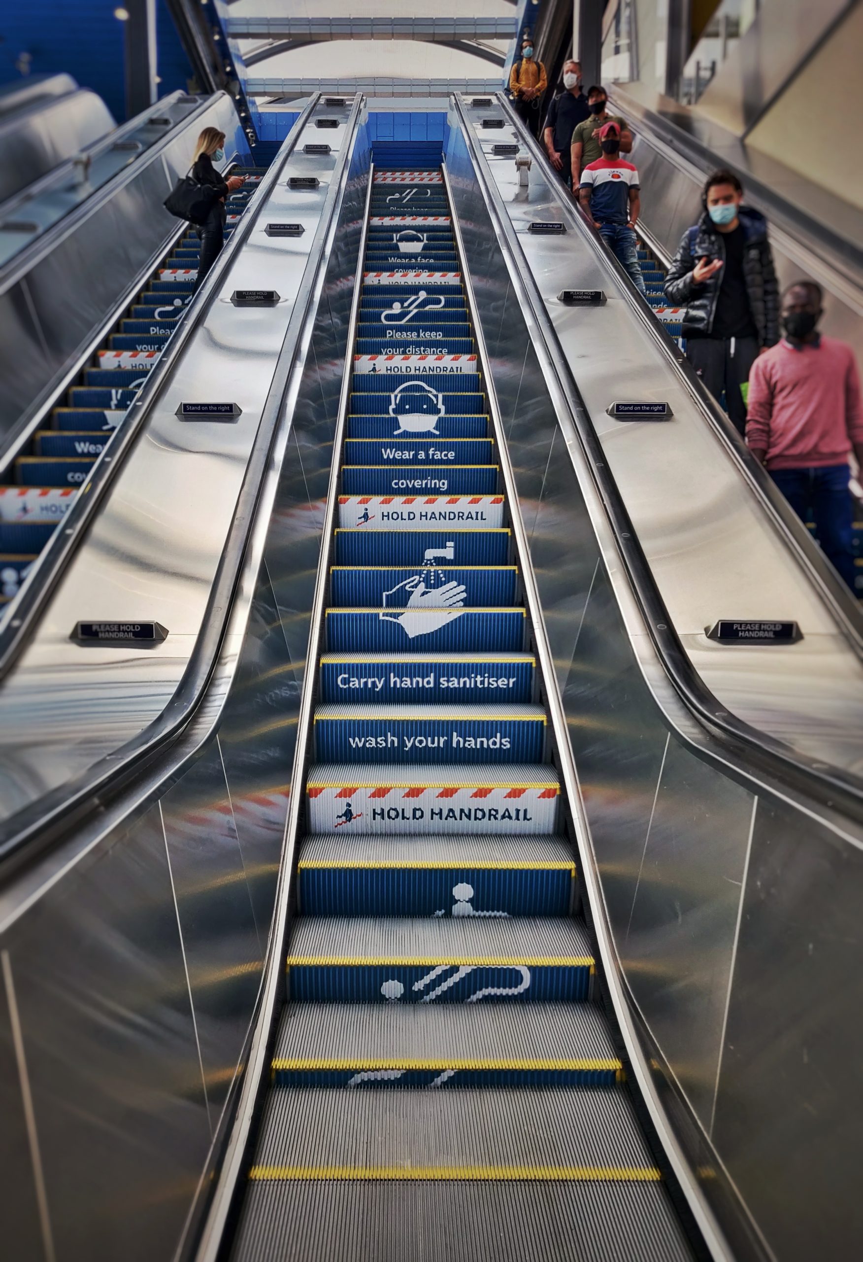 An escalator on the London underground is adorned with warning signs about social distancing and COVID-19 as travellers in face masks stay distanced