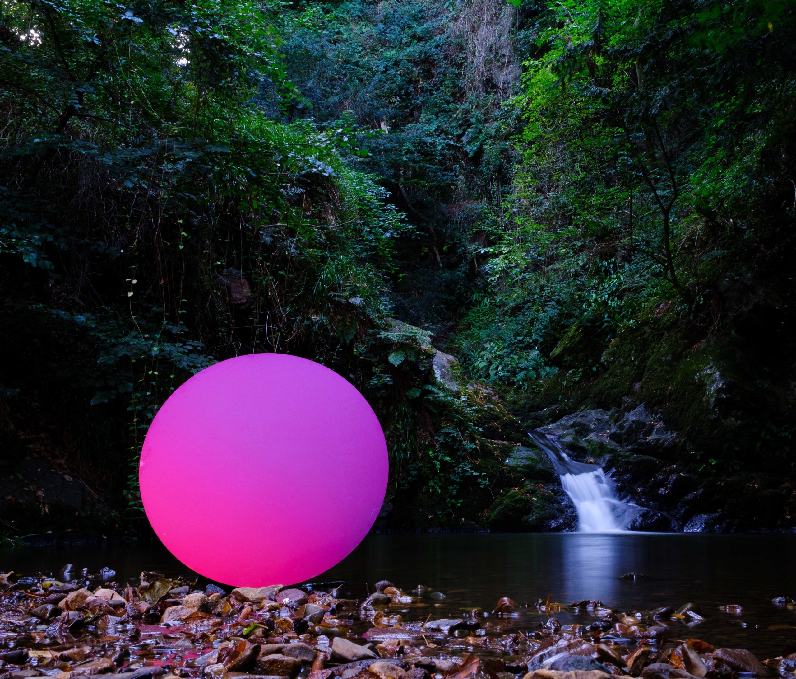 An orb of purple Pure Structural Colour placed in front of a waterfall