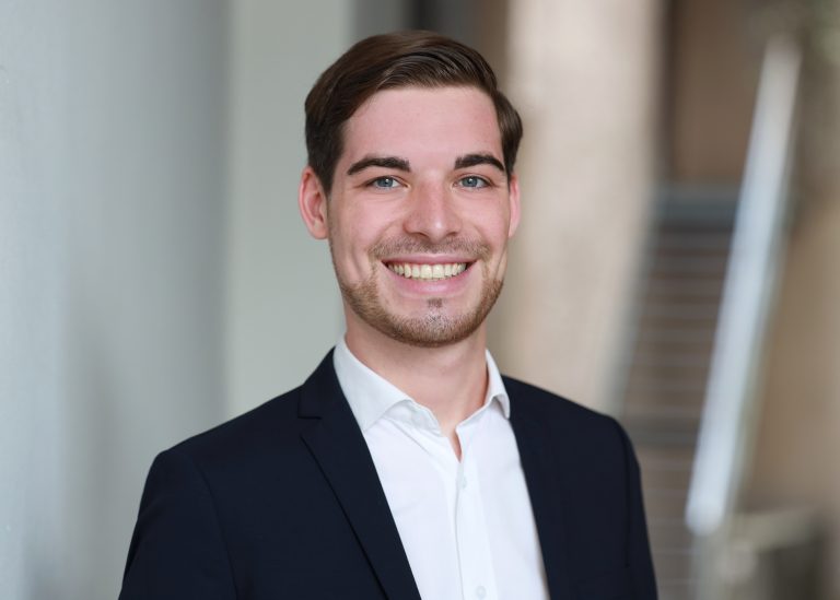 Marcel Schana smiling broadly, wearing a white shirt and black jacket