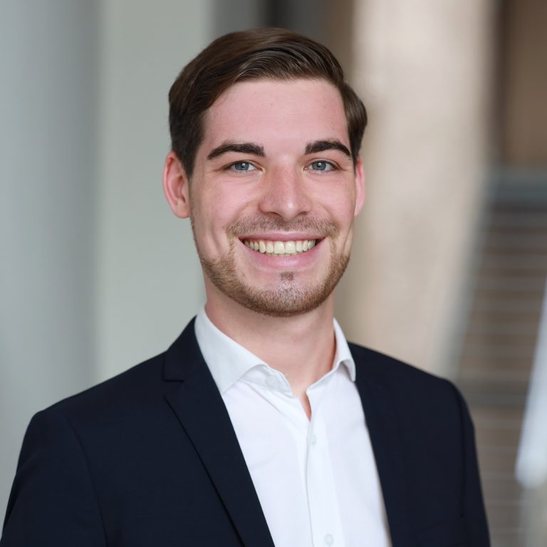 Marcel Schana smiling broadly, wearing a white shirt and black jacket