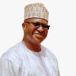 prof.muhammadou Kah in front of a white background. They wear glasses and a hat