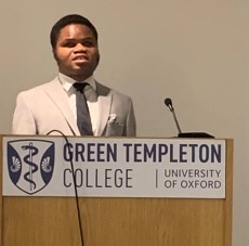 Ebenezer Azamati in cream suit and dark tie speaking at lectern