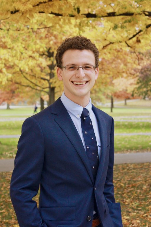 Andrew Rosenblatt wearing a navy suit stood infront of an autumnal tree
