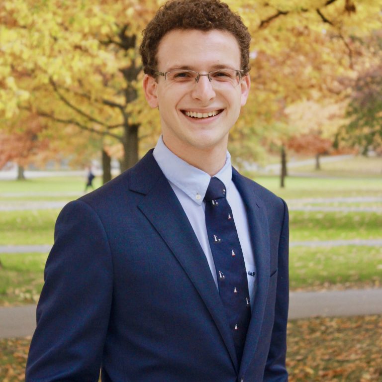 Andrew Rosenblatt wearing a navy suit stood infront of an autumnal tree