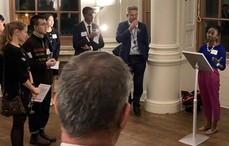 Speaker behind lectern giving remarks with a small number of smartly dressed guests in view