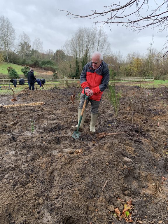 Derek Jewell in red coat and wellies digging with spade
