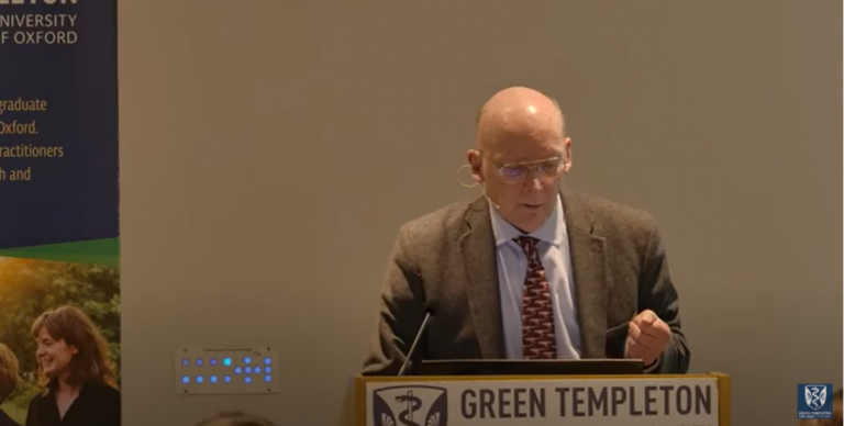 Charles Godfray standing behind lectern wearing brown suit jacket