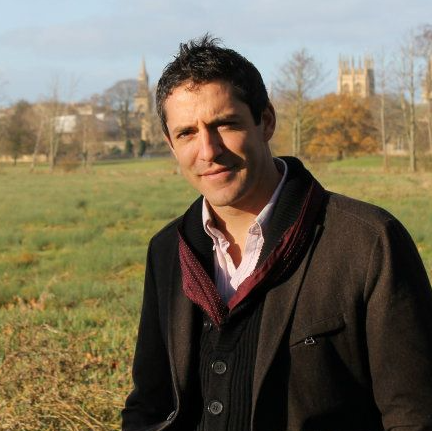 Jacob Mcknight portrait outside in dark coat with grassy meadow behind
