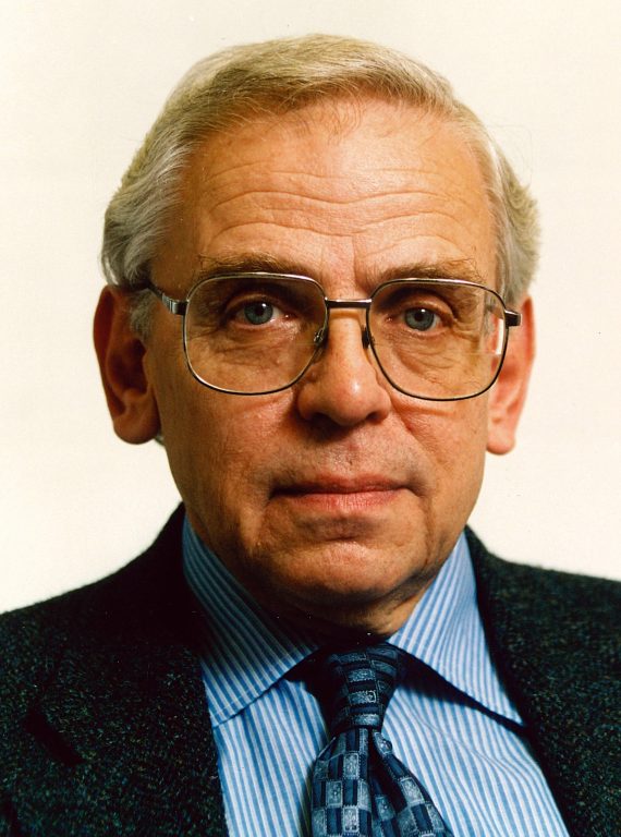 Roger Undy portrait in dark jacket and blue shirt and tie with glasses