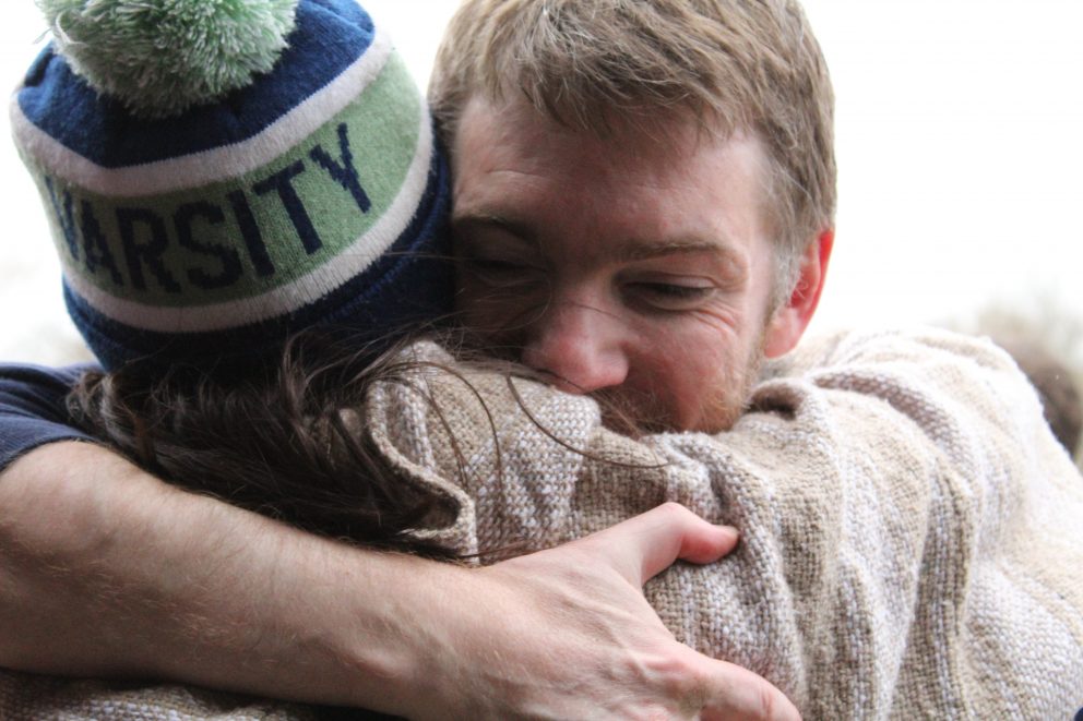 Tightly framed image of two individual embracing one another, one with hand on others back