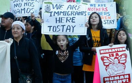 Men, women and children hold posters saying 'We are immigrants here to stay' as they take part in a demonstration