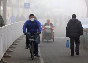 Members of the public wear masks as they cycle across a smoggy bridge