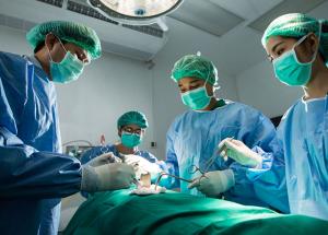 Three surgeons and an anesthetist stand over a patient in an operating theatre