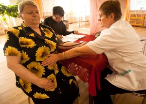 A community nurse leans over to feel a patient's stomach at a community clinic