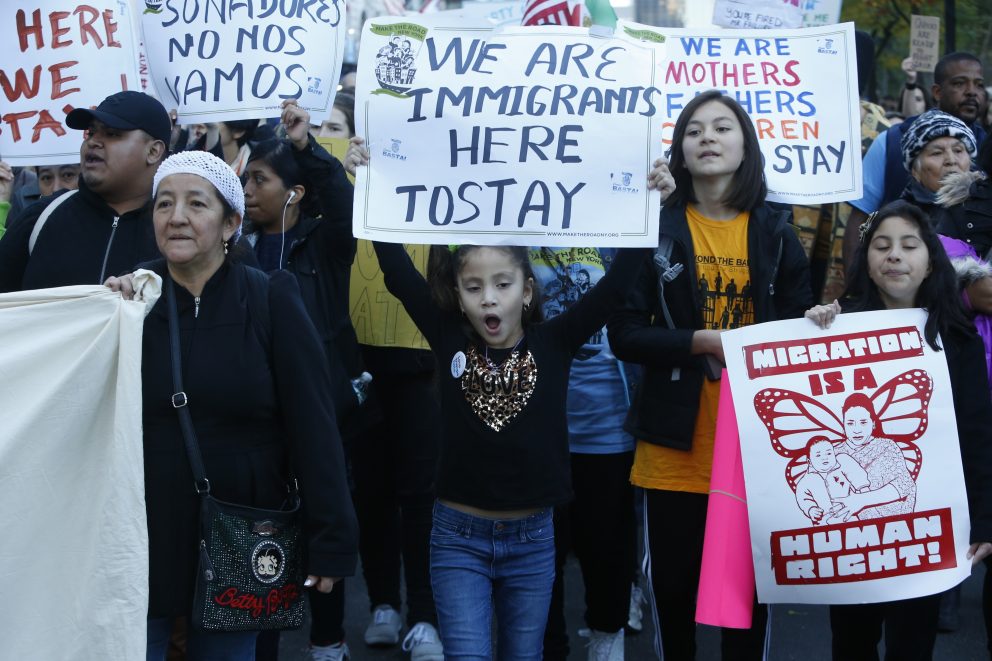 Men, women and children take part in a demonstration holding signs that say 'We are immigrants here to stay'