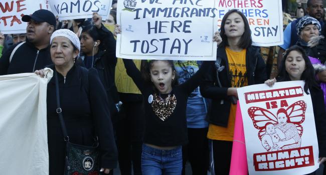 Men, women and children hold placards supporting migration as they gather in the street
