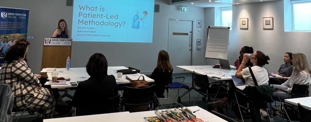 Patient Led Methodology Workshop Setup With Big Screen And Participants Seated Around Tables