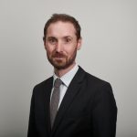 Adam Briggs wearing suit in front of grey wall