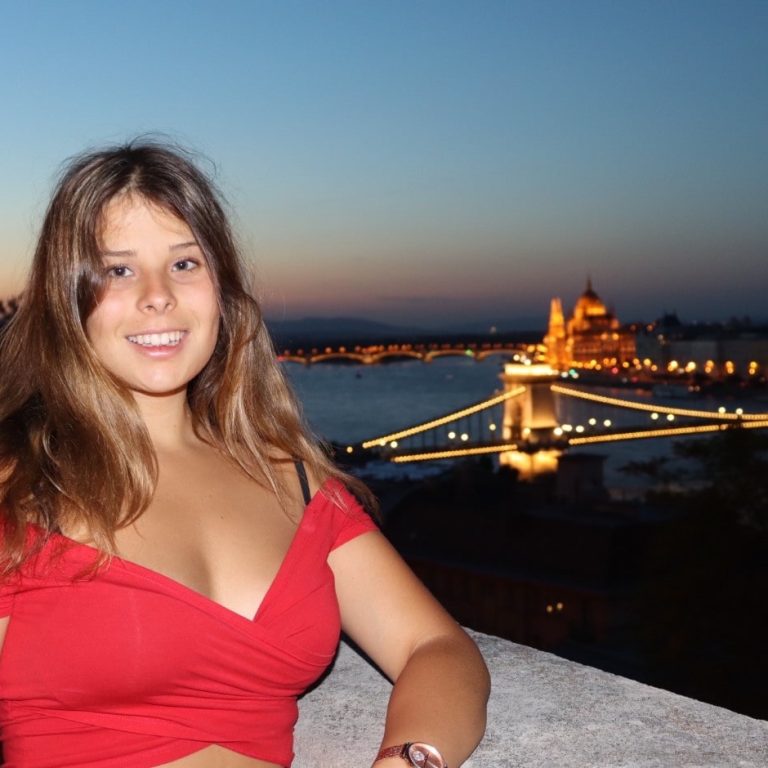 Dorottya Zsiboracs at dusk in front of river with golden city lights in background