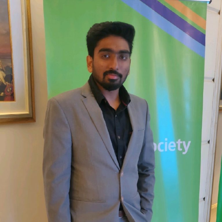 Harsha Vardhan Puli in front of green sign wearing grey suit