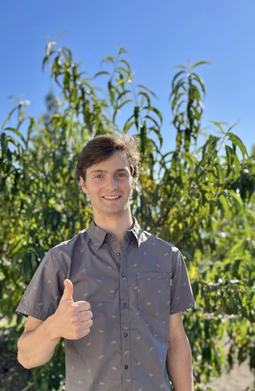 Isaac Rankin with thumb up in front of a green tree with blue skies