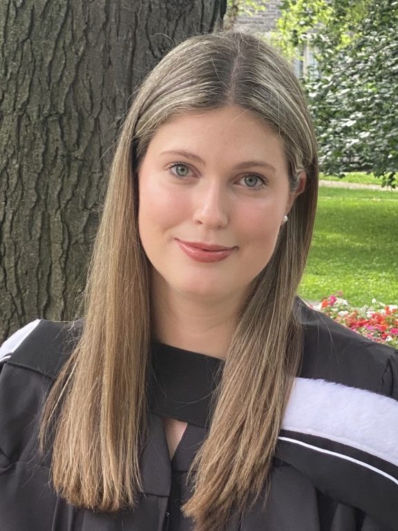 Mathea Treslan wearing graduation roles in front of a tree