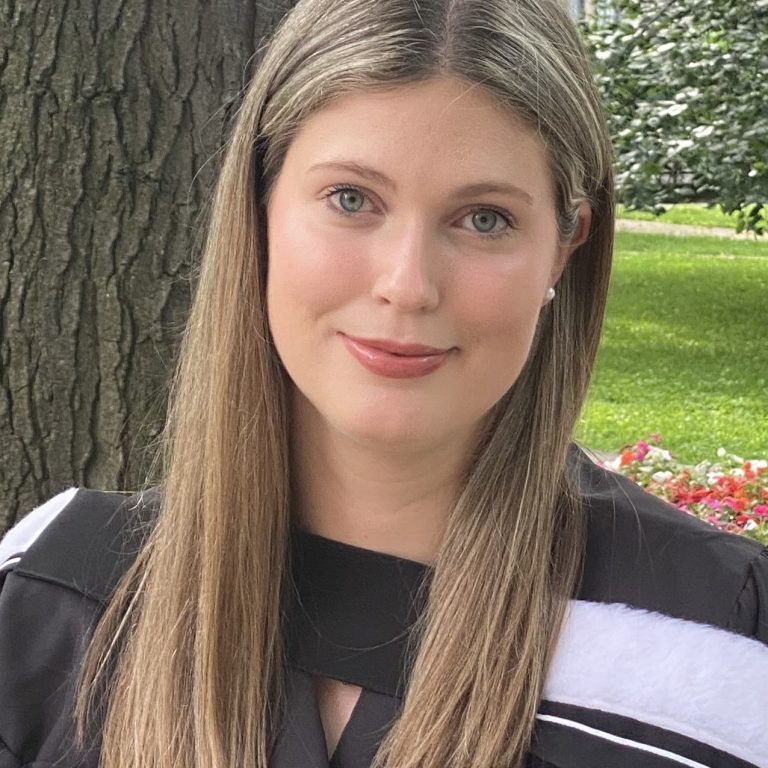 Mathea Treslan wearing graduation roles in front of a tree