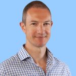 Richard White Profile Pic In Open Neck Blue And White Checked Shirt With Plain Blue Background