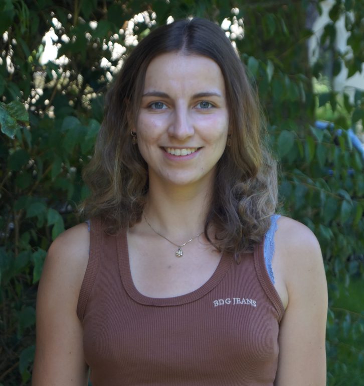 Katharina Neumann stood in front of green bushes wearing a brown top