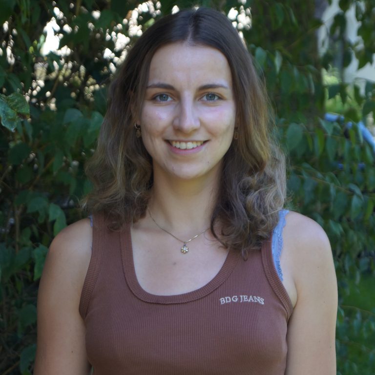 Katharina Neumann stood in front of green bushes wearing a brown top
