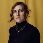 Elisa Sai wearing black high neck top in front of Yellow background