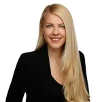 Helen O'neill in front of white background wearing black blazer with long blonde hair over left shoulder. 