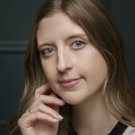 Tori Ford with hand by face in front of grey back ground