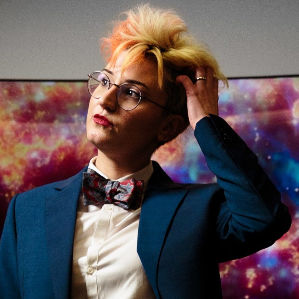 Dr Heloise Stevance profile pic in bow tie and blue jacket with left hand on side of head