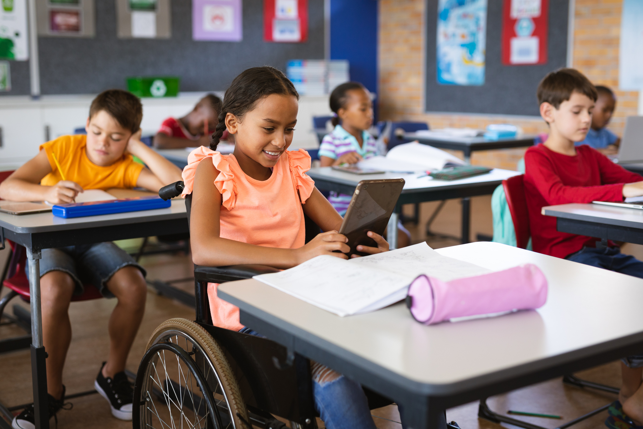 Disabled African American Girl Using Digital Tablet While Sitting On Wheelchair At Elementary School