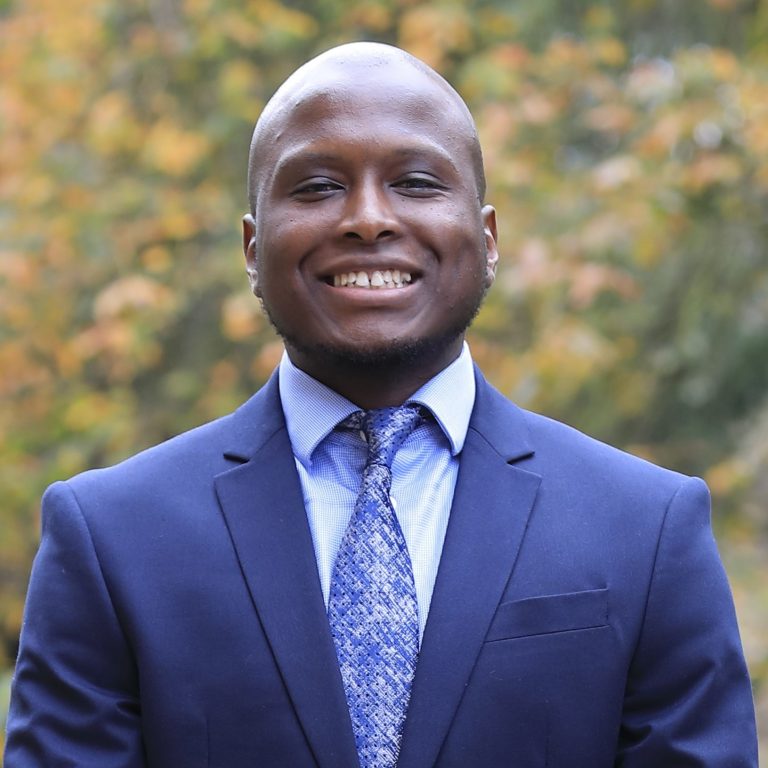 Brendon Mahere headshot wearing blue suit in front of greenery