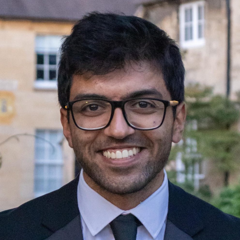 Shubh Kumar smiling at camera wearing suit and glasses