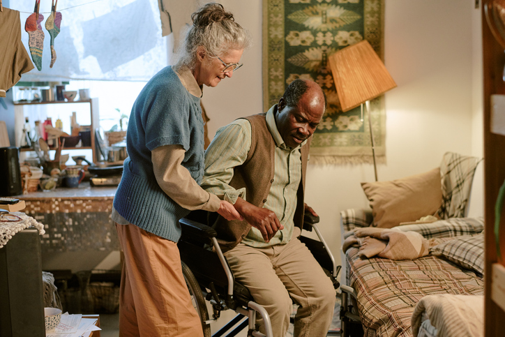Senior Caucasian Woman Assisting Senior Black Man With Disability Standing Up
