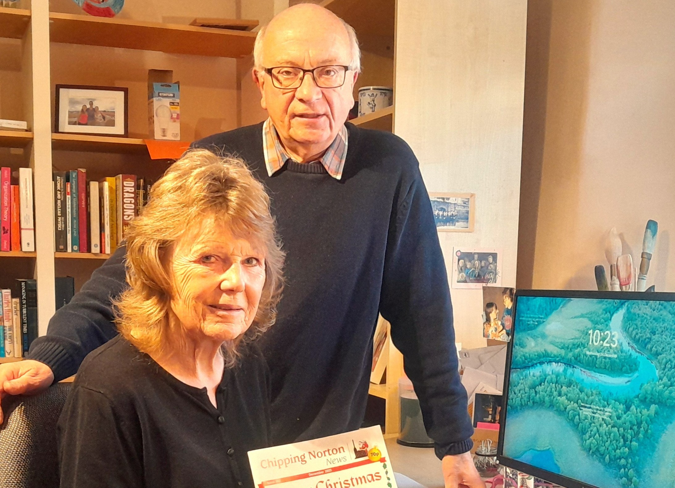 Keith Ruddle and Jill Thorley by computer monitor with newsletter in hands