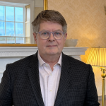 Sir Michael Dixon in front of Fireplace looking at camera