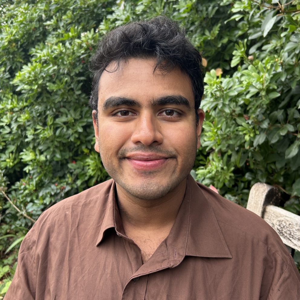 Kapil Narain Seating On Bench Outside With Green Bush Behind